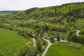 Luftbildaufnahem auf einen Parkplatz/Wohnmobilstellplatz bei Distelhausen. Daneben ist eine Kapelle und ein Friedhof zu sehen.  Es ist ein idyllischer Ort an der Tauber, mit Wiesen und bewaldeten Hügeln.