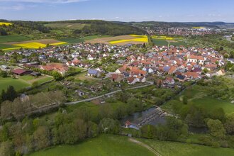 Luftbildaufnahme auf den Stadtteil Dittigheim, umrahmt von Wiesen, Feldern und Bäumen. Im Hintergrund ist die Stadt Tauberbischofsheim zu sehen.