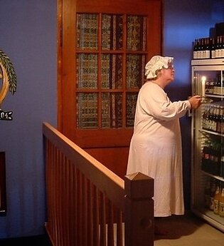 Eine Peson steht in Nachthemd und Mütze vor einem Kühlschrank mit Getränken