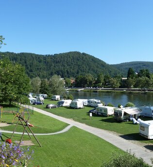 Campingplatz mit einer Reihe von weissen Wohnwägen. Direkt am Platz vorbei fliesst ein Fluss, der Neckar. Im Hintergrund ein bewaldeter Berg. Eberbach im Odenwald.