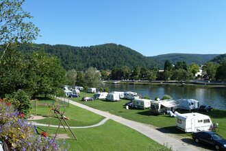 Campingplatz mit einer Reihe von weissen Wohnwägen. Direkt am Platz vorbei fliesst ein Fluss, der Neckar. Im Hintergrund ein bewaldeter Berg. Eberbach im Odenwald.