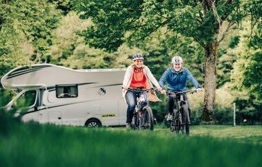 Zwei Radfahrer im Hintergrund ein weißes Wohnmobil und Bäume. Odenwald.