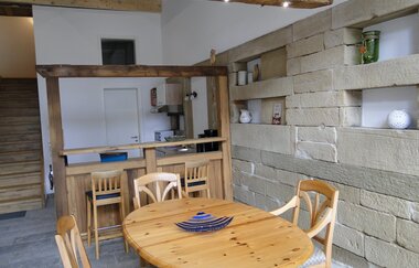 Im Esszimmer steht ein Holztisch mit Stühlen vor einer rustikalen weiß gestrichenen Mauer