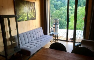 Im Wohnzimmer steht eine hellgraue Couch und die Tür geht hinaus ins Grüne