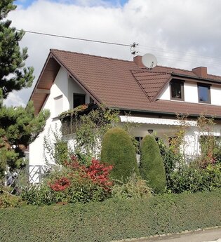 Das Gästehaus ist außen umgeben von vielen grünen Sträuchern.