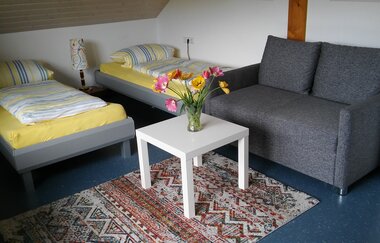In einem Gästezimmer gibt es zwei Betten, ein Sofa und ein Beistelltisch.