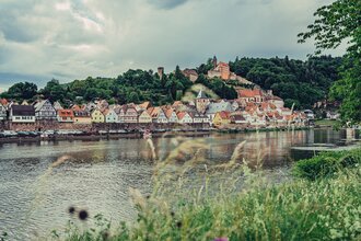 Ein Fluß (Neckar). Au fder anderen Uferseite ist eine Stadt zu sehen. Auf einem Berg ein Schloss. Hirschhorn im Odenwald.