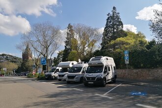 Vier Wohnmobile parken auf Stellplätzen an einer Schlossmauer, ein Behindertenparkplatz ist leer