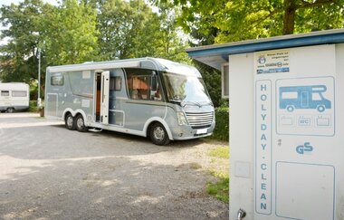 Auf einem Platz steht ein graues Wohnmobil. Dahinter sind Bäume zu sehen. Im Vordergrund stehe eine Clean-Station. Walldürn im Odenwald.