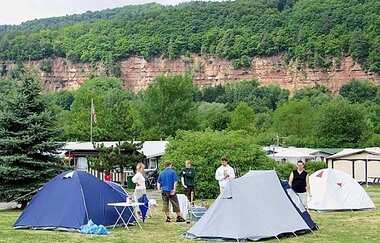 Blick auf Zelte auf dem Seecamping-Platz in Freudenberg. Im Hintergrund sind Felswände aus rotem Sandstein und Wald zu sehen.