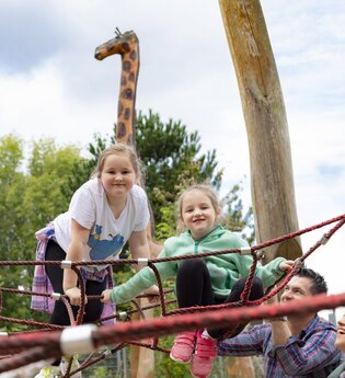 2 Kinder auf einem Klettergerüst. Die Eltern stehen davor. Im Hintergrund ist ein lebensgroße Holzgiraffe. Schwarzach im Odenwald.