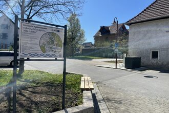 Eine Informationstafel im Vordergrund. Auf der rechten Seite steht ein Haus. Haßmersheim i Odenwald.