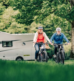 Zwei Radfahrer im Hintergrund ein weißes Wohnmobil und Bäume. Odenwald.