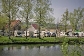 Blick auf den direkt an der Tauber gelegenen Wohnmobilstellplatz in Röttingen. Der Platz ist gut besucht. Im Hintergrund sind Häuser zu sehen.