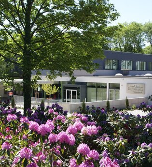 Blick auf Gebäude, die Katzenbuckel-Therme, davor eine Blumenfeld mit rosa und lila farbenen Blumen. Waldbrunn im Odenwald.