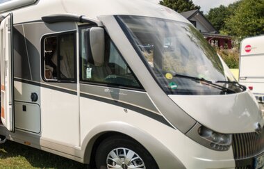 Frontansicht eines geparkten, modernen Wohnmobils mit großen Fenstern auf einer grünen Wiese.