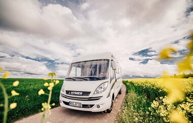 Ein weißes Wohnmobil. Auf der linken Seite eine großes grünes Feld. Auf der rechten Seite ein gelbes Rapsfeld. Odenwald.