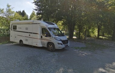 Ein weißes Wohnmobil im Schatten von Bäumen auf einem geschotterten Platz. Elztal im Odenwald.