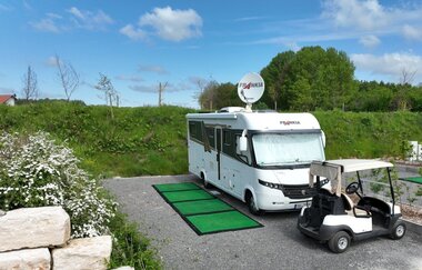 Ein weißes Wohnmobil, davor ein weißes Golfcart. Ein grüner Teppich liegt davor. Im Hintergrund eine grüne Wiese mit Bäumen. Mudau im Odenwald.