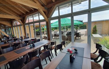 Ein Restaurant mit Tischen und Stühlen und großen Fenstern. Blick auf einen Biergarten mit grünen Schirmen. Mudau im Odenwald.