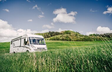 Ein weißes Wohnmobil inmitten von grünen Wiesen. Im Hintergrund ein bewaldter Hügel. Odenwald.