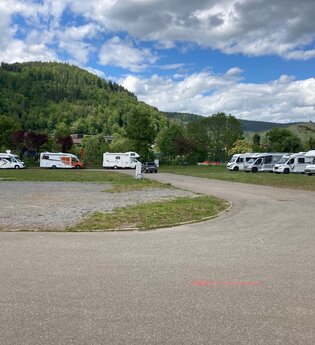 Eine geschotterte Fläche. Auf der linken Seite sowie auf der rechten Seite des Platzes stehen jeweils 4 Wohnmobile. Im Hintergrund ist ein bewaldeter Berg. Eberbach im Odenwald.