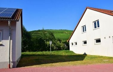Blick auf einen Wohnmobilstellplatz in Markelsheim, eine Grünfläche zwischen zwei Gebäuden. Im Hintergrund sind die Weinberge zu sehen.