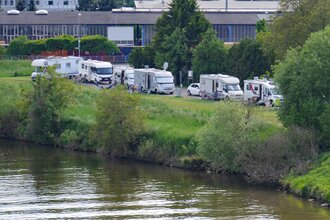 Ein Fluß an dessen Ufer ein Wohnmobilstellplatz ist. Es stehen mehrere Stellplätze in Reihe auf einer Wiese. Obrigheim im Odenwald.