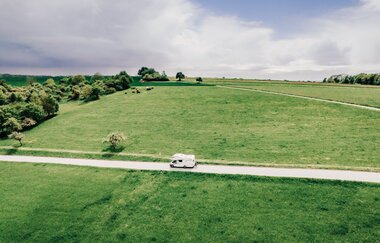 Man sieht eine Strasse mit einem weißen Wohnmobil.  Auf beiden Seiten der Strase sind grüne Wiesen. Odenwald.