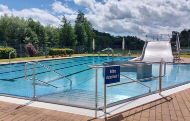 Es ist ein Freibad mit einer Treppe zu sehen. Auf der anderen Seite des Bads gibt es eine breite Stahlrutsche. Schefflenz im Odenwald