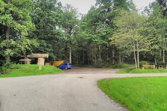 Ein Parkplatz am Waldrand. Auf dem Platz stehen zwei Fahrzeuge. Davor führt ein Weg vorbei. Schönbrunn im Odenwald.