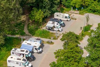 Wohnmobilstellplatz mit mehreren geparkten Wohnmobilen, umgeben von Bäumen.