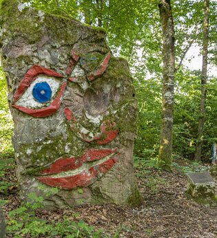 Ein großer Baumstumpf mit einem aufgemalten Gesicht im Wald. Seckach im Odenwald.