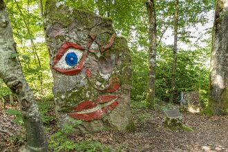 Ein großer Baumstumpf mit einem aufgemalten Gesicht im Wald. Seckach im Odenwald.