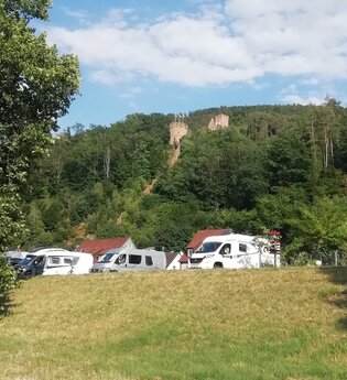 Blick auf den Wohnmobilstellplatz am Stadteingang Süd in Freudenberg am Main. Im Hintergrund ist von Wald umgeben die Freudenburg zu sehen.