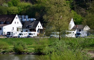 Blick auf den Wohnmobilstellplatz am Main in Freudenberg. Im Hintergrund sind Häuser und Wald zu sehen.