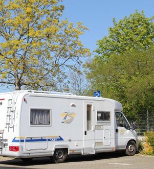 Blick auf den Wohnmobilstellplatz in Tauberbischofsheim. Hier ist ein Wohnmobil neben Bäumen auf einem asphaltierten Platz zu sehen.
