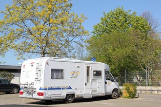 Blick auf den Wohnmobilstellplatz in Tauberbischofsheim. Hier ist ein Wohnmobil neben Bäumen auf einem asphaltierten Platz zu sehen.