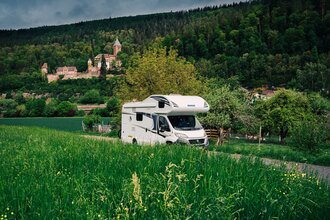 Im Vordergrund ist eine grüne Wiese mit einem Wohnmobil zu sehen. Im Hintergrund ein Schloss. Es handelt sich um das Schloss Zwingenberg am Neckar im Odenwald.