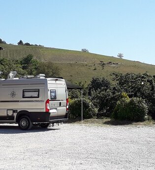 Wohnmobil auf einem Schotterplatz bei gutem Wetter mit Weinbergen im Hintergrund