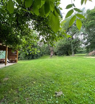 Blick auf den Wohnmobilstellplatz auf dem Ferienbauernhof Schamman in Neubronn. Es ist eine von Bäumen umgebene Wiese mit einer Pergola zu sehen.