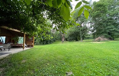 Blick auf den Wohnmobilstellplatz auf dem Ferienbauernhof Schammann in Neubronn. Es ist eine von Bäumen umrandete Wiese und eine Pergola zu sehen.
