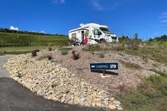 Blick auf den am Rand der Weinberge gelegenen Wohnmobilstellplatz Weingut Ehrmann.  Hier steht ein Wohnmobil. Bei schönstem Wetter und blauem Himmel genießen die im Freien sitzenden Gäste den Ausblick.
