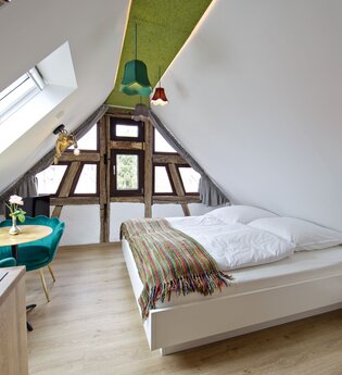 Schlafzimmer mit Doppelbett und einem kleinen Tisch mit zwei bequemen türkisfarbenen Stühlen