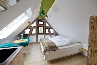 Schlafzimmer mit Doppelbett und einem kleinen Tisch mit zwei bequemen türkisfarbenen Stühlen