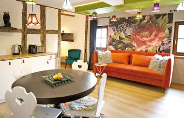 Wohnraum mit großer orangefarbener Couch und einem runden Hooltisch mit vier Stühlen