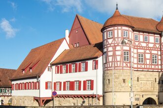 altes Schloss - rechts das Torhaus mit Sockelgeschoss aus hellem Sandstein und aufgesetztem roten Fachwerk mit weißen Gefachen, flankiert von zwei Rundtürmen. In der Bildmitte der Westflügel mit zwei aneinandergebauten, weiß verputzten Gebäudeteilen mit r
