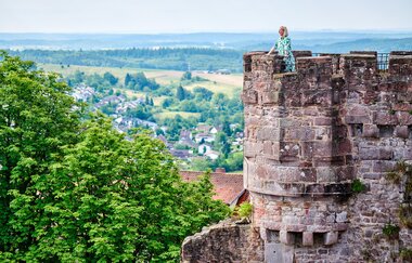 Eine Frau steht auf einem Burgturm und genießt die Aussicht über den Odenwald.