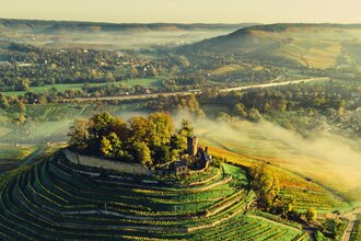 Drohnenaufnahme der Burgruine Weibertreu im Morgennebel. Aussicht über Weinsberger Tal mit dem Naturpark Schwäbisch-Fränkischer Wald im Hintergrund.
