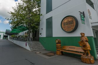 Blick auf den Eingangsbereich der Distelhäuser Brauereigaststätte. Hier steht eine große hölzerne Bank mit einer geschnitzten Figur, die einen Bierkaste trägt. An der Wand hängt ein geschnitzer Fassboden. Im Hintergrund ist die Terasse zu sehen.